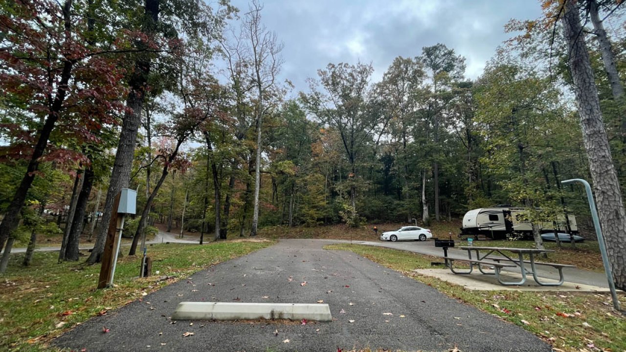 Autumn day at a campground with RV parking spot, picnic table, and vehicles.