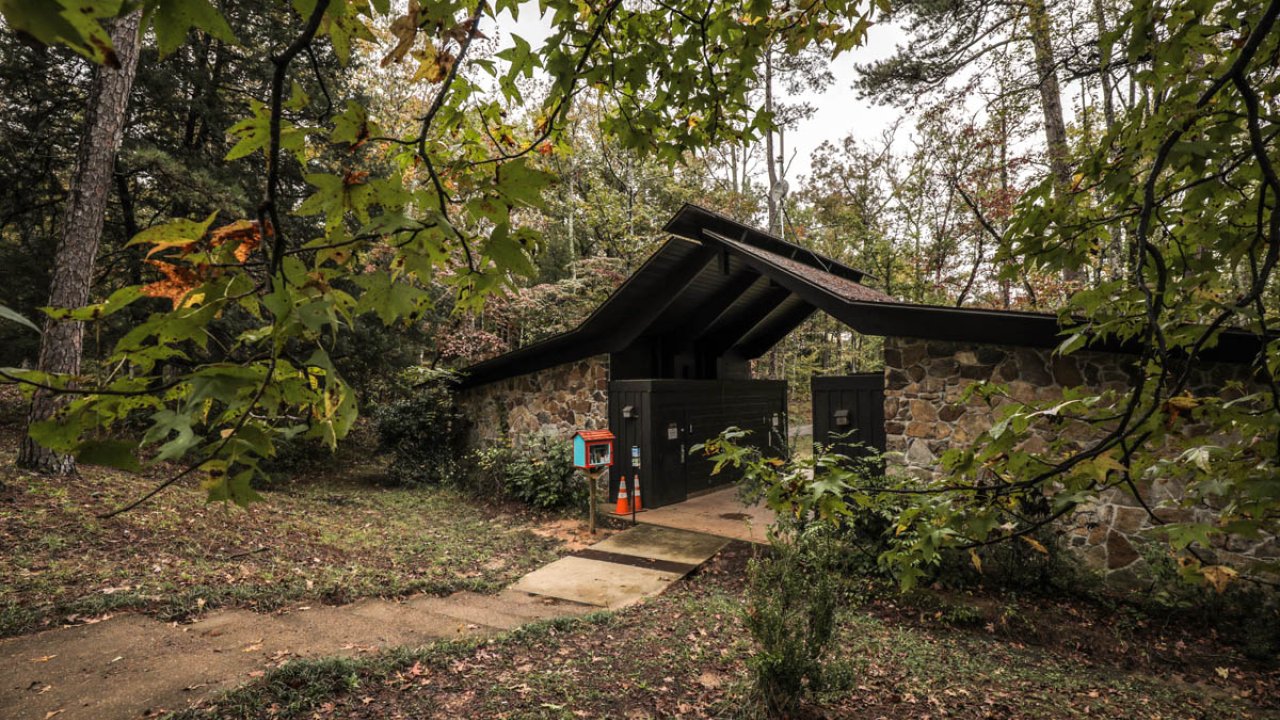 Small stone cabin with dark roof in a forest setting.