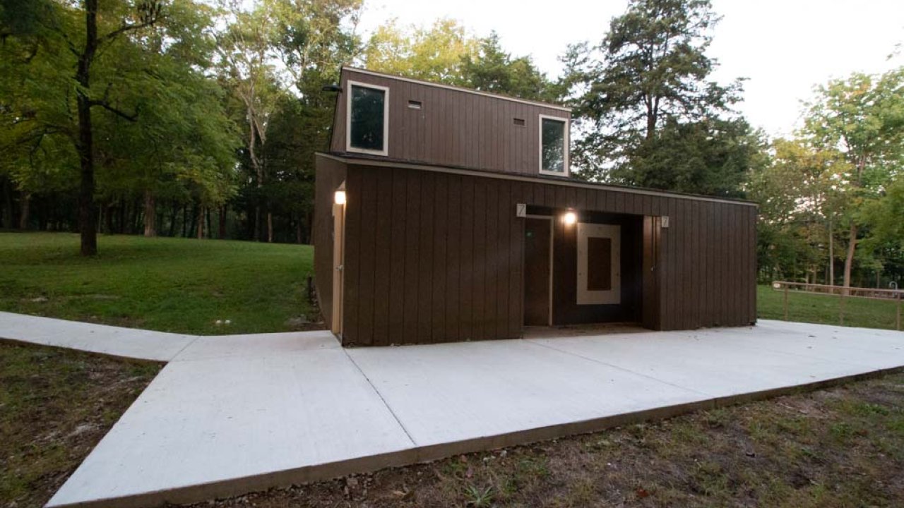 Modern small house with brown siding in a forest clearing at dusk.