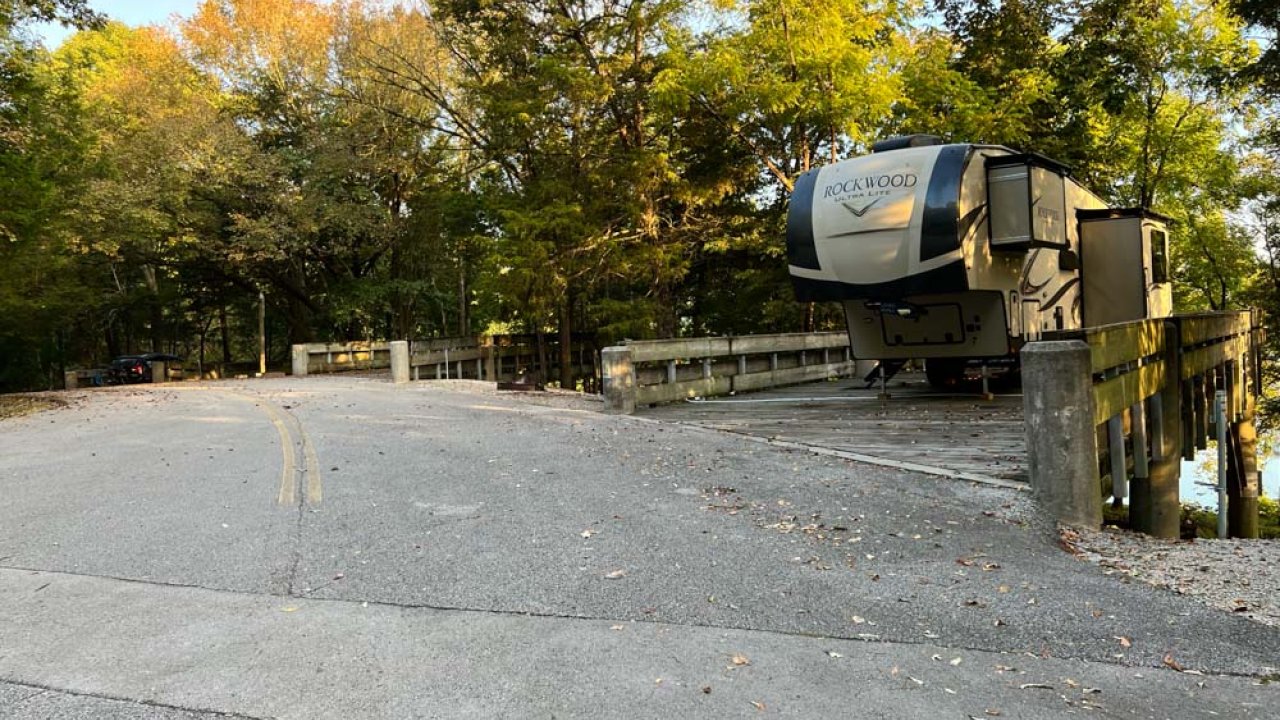 RV parked beside a wooden fence in a shaded park area.