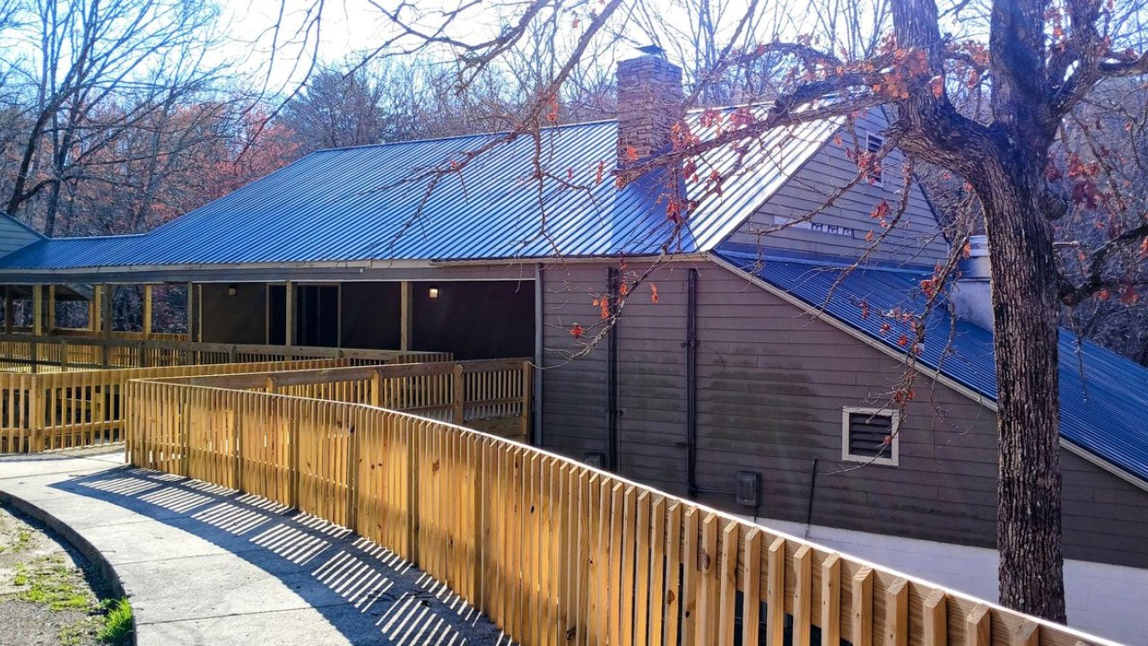 Brown house with a wooden ramp, surrounded by bare trees, under a bright blue sky.