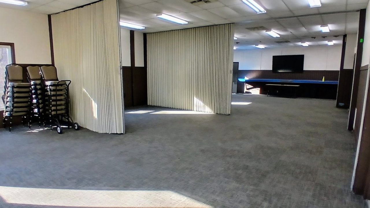 Wide meeting room with stackable chairs and closed divider curtains.