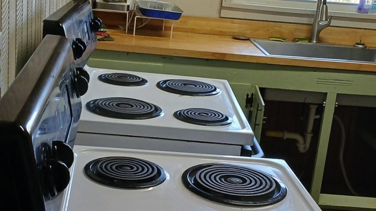 Stove with coil burners in rustic kitchen with wooden walls and window.
