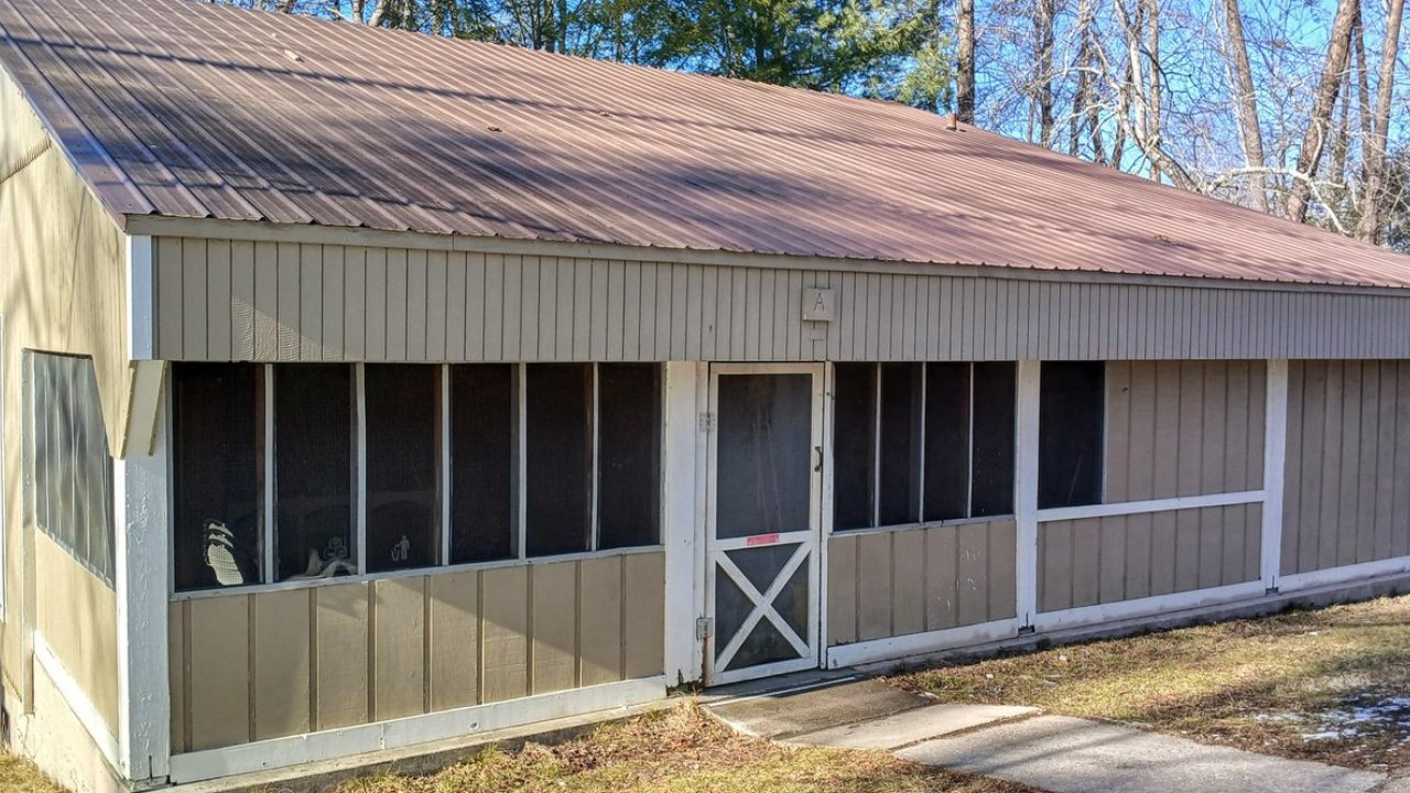 Tan cabin with screened windows in a wooded area.