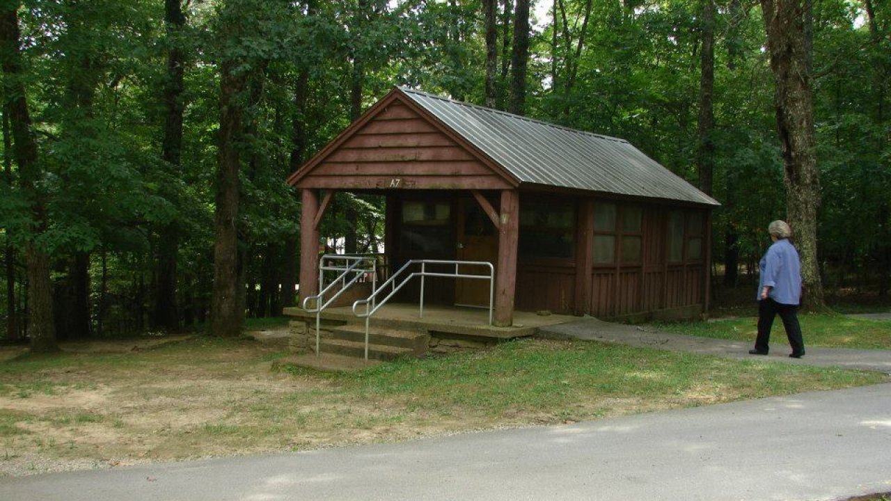 A small brown cabin in a wooded area with a person walking nearby.
