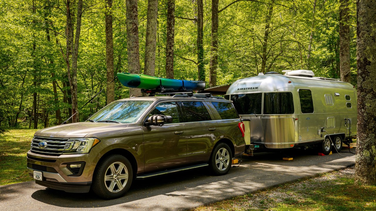 SUV towing an Airstream trailer in a lush green forest.