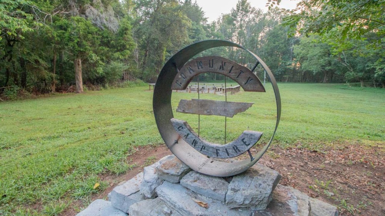 Circular metal sculpture on stone base in a misty park.