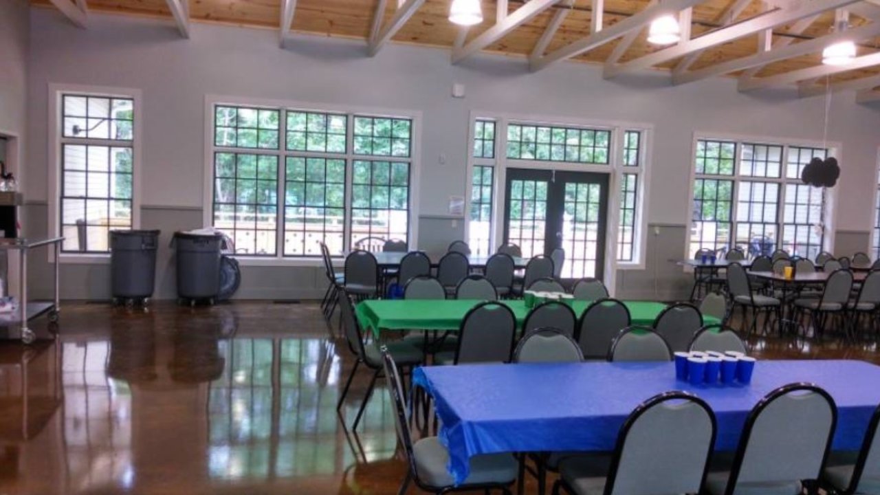 Bright hall with tables covered in blue and green cloths, large windows, and high ceiling.