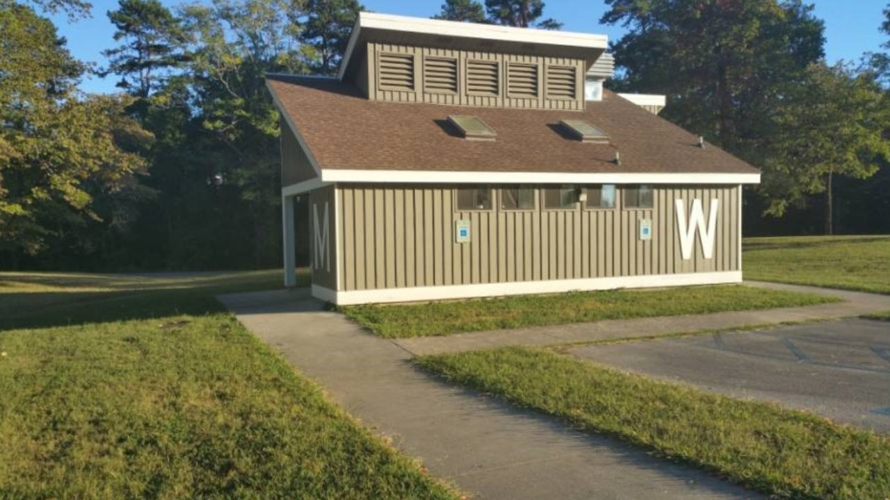 Small brown building with a sloped roof in a grassy area.