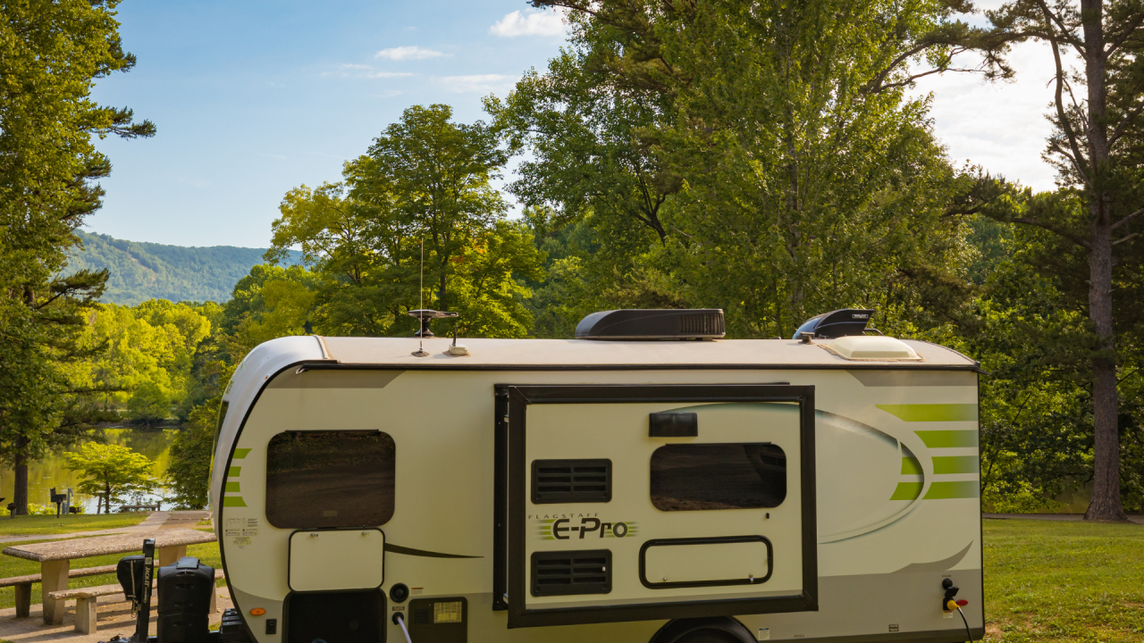 Travel trailer parked in nature with trees and mountains in the background.