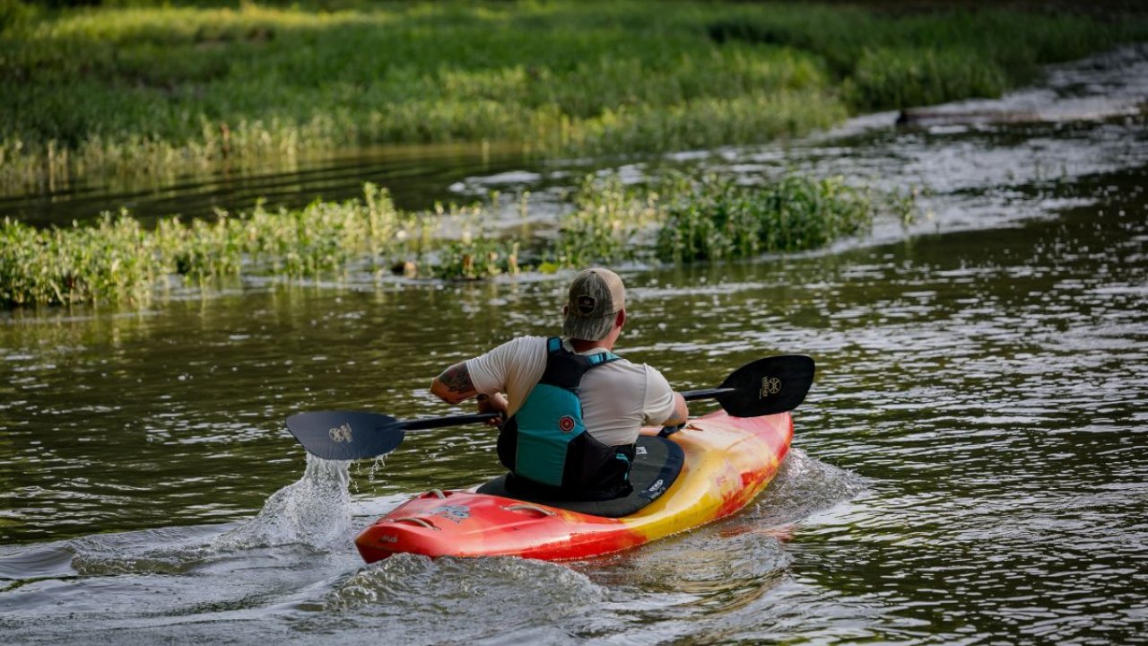 Person kayaking along a calm river with lush greenery.