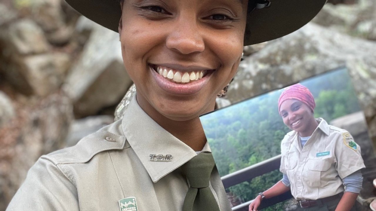 Park ranger smiling, holding a photo of themselves, outdoors.