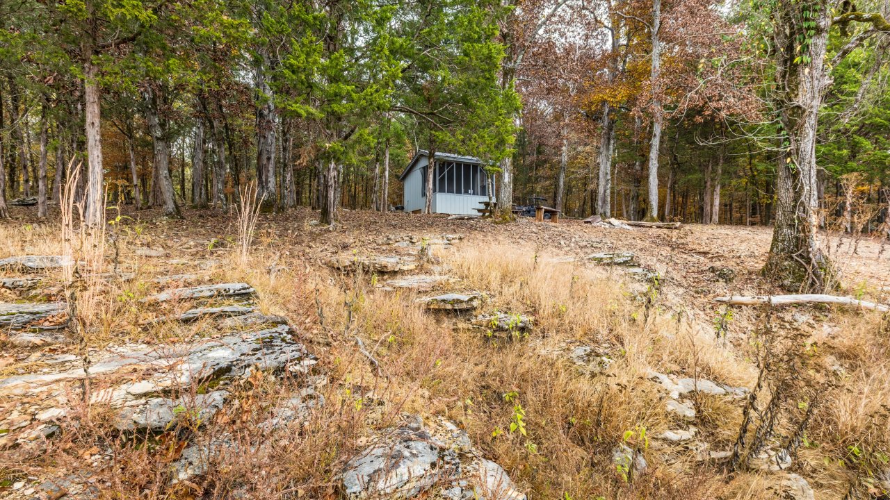 Small cabin in a wooded, rocky clearing during fall.