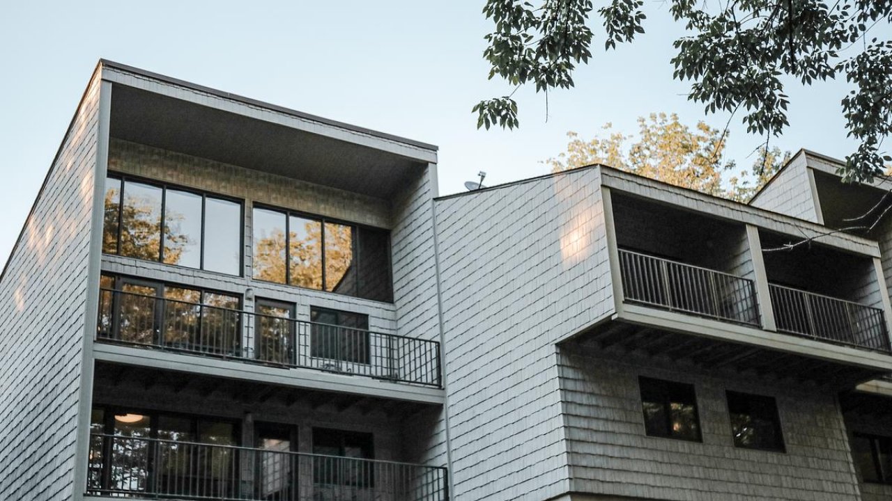 Modern apartment building with large windows and balconies, trees in the background.