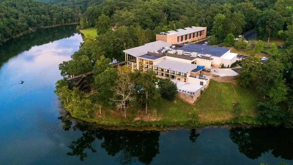 Aerial view of a riverside building surrounded by lush green forest.