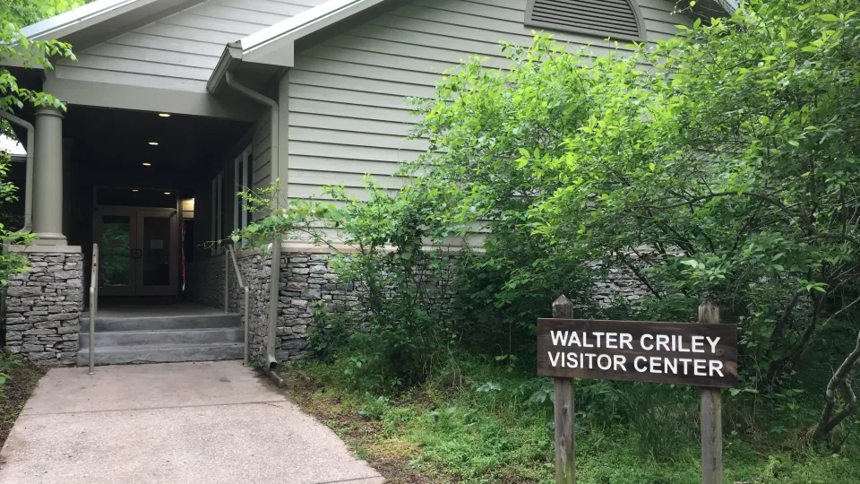 Visitor center with a wooden sign surrounded by greenery.