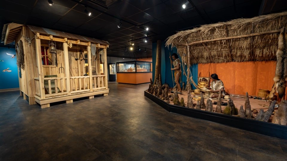 Exhibit of a wooden cabin and indigenous hut in a museum setting.