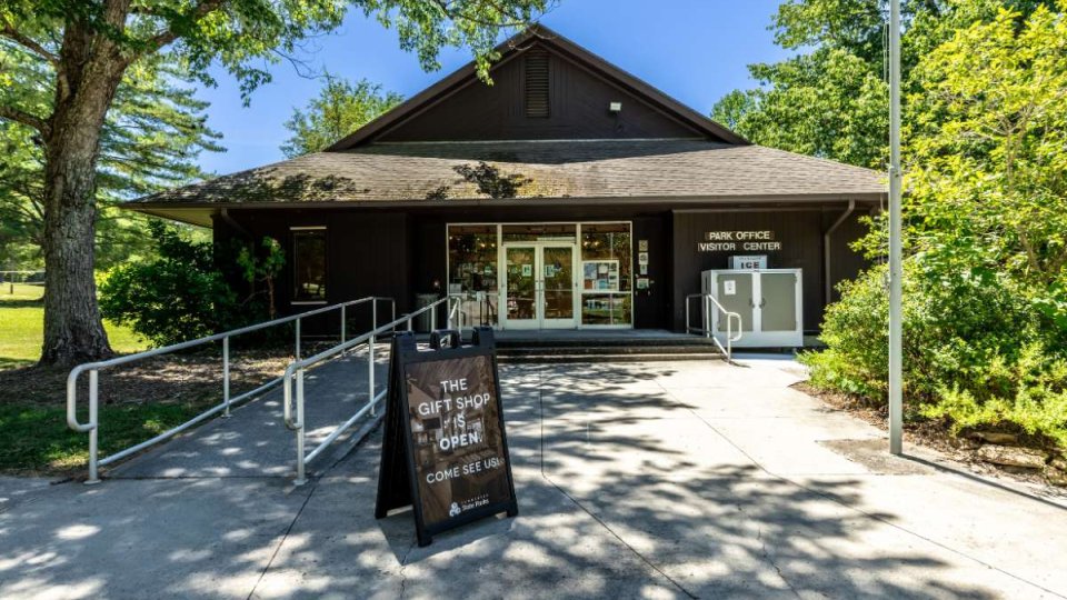 Brown building with a ramp and stairs leading to it, a sign is in front that says the gift shop is open