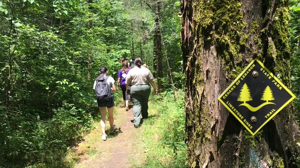 people walking down a tight path in the forest with a sign that says cedars of Lebanon trail