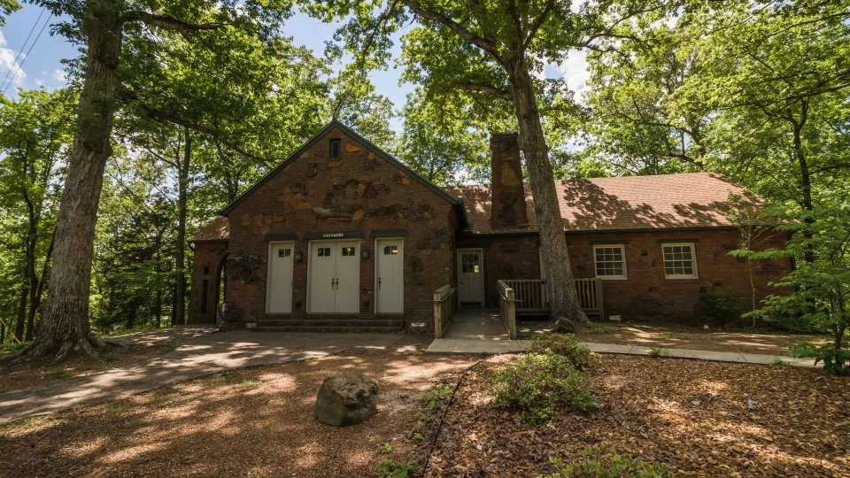 Rustic brick lodge in a forest setting, surrounded by tall trees and sunlight.