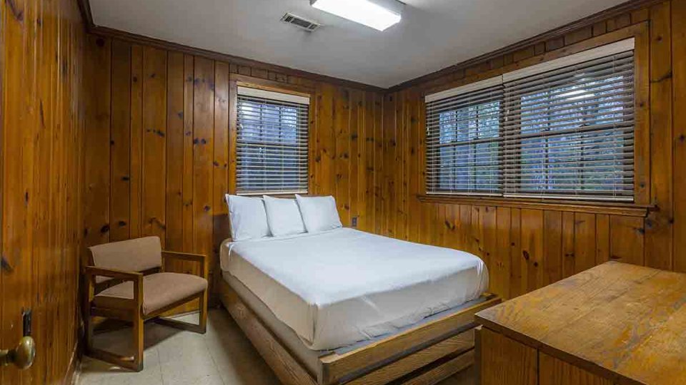 Wooden bedroom with one bed, a chair, a dresser, and windows