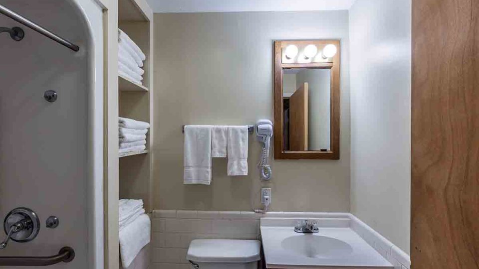 Bathroom with toilet, single sink, small mirror, white towels, and shower