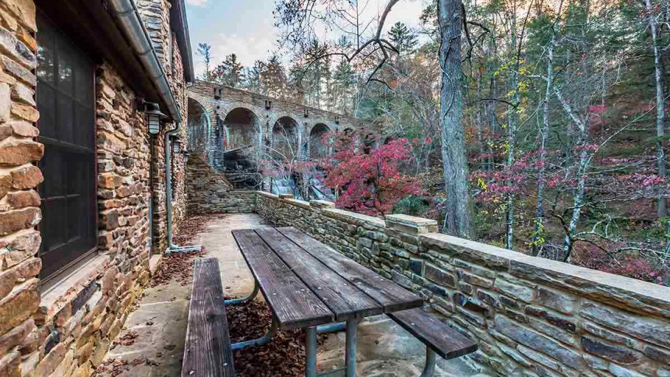 stone patio with wooden picnic table that has view of woods and bridge