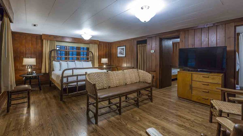 wooden living room with chairs, bench, dresser, single king sized bed, two night stands, and two lamps