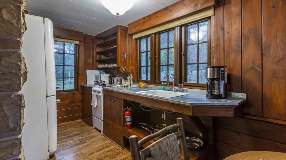 wooden kitchen with white refrigerator, white stove, sink, coffee maker, kitchen table, chair, and windows