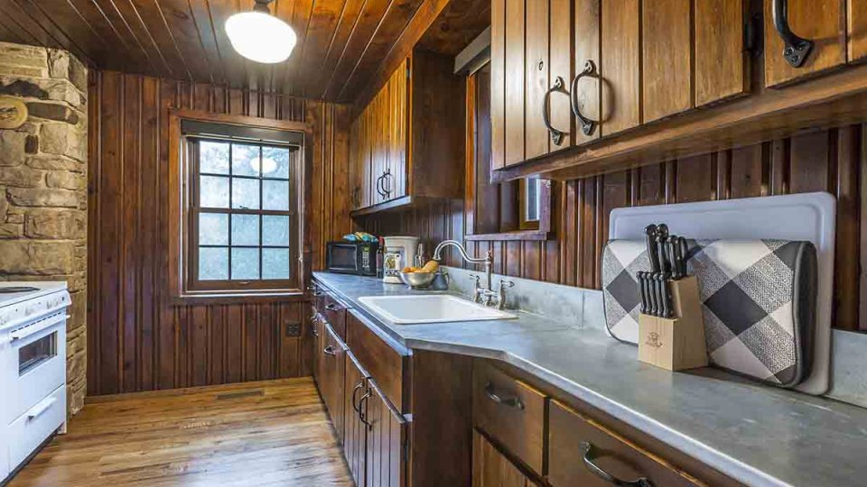 Wooden kitchen with gray countertops, kitchen knives, sink, stove top, cabinets, and windows