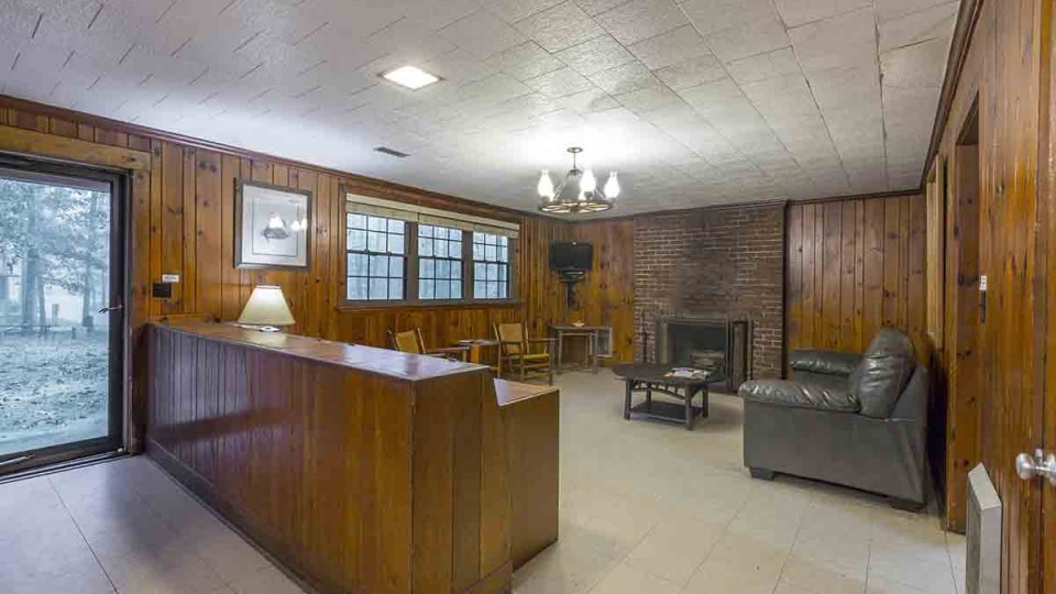 Wooden living room with door that goes outside, windows, fireplace, couch, chairs, coffee table, chandelier, lamp, mounted television in corner, and overhead lighting 