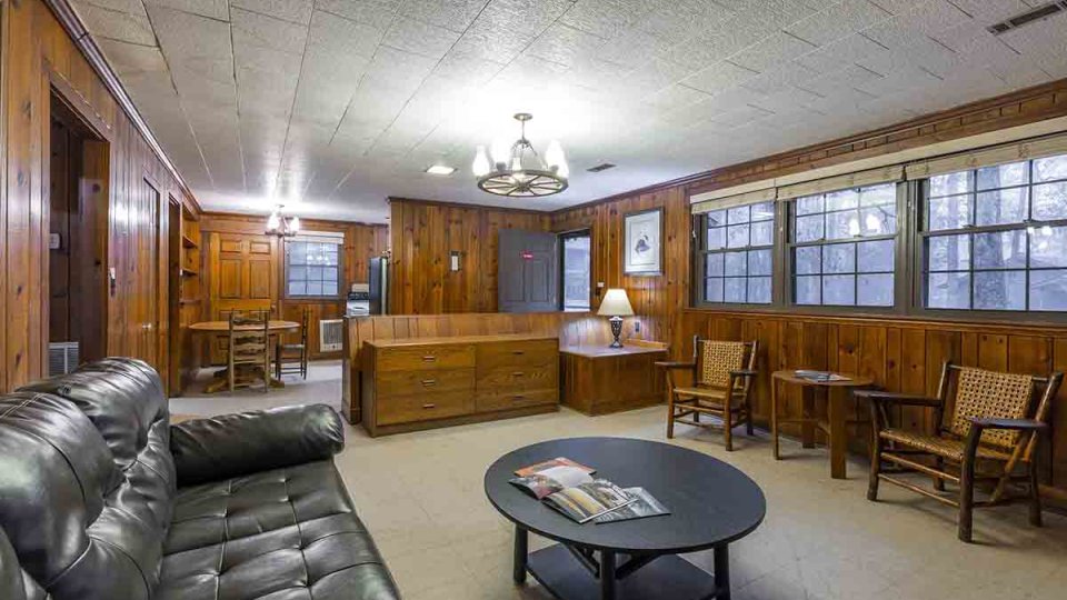 Wooden living room with couch, coffee table, chairs, lamp, windows, chandelier, and dining table