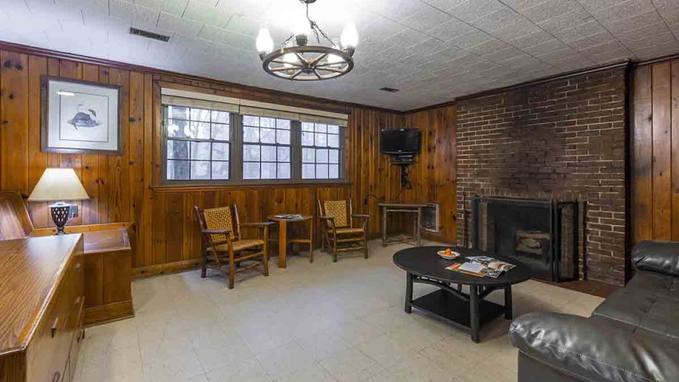 Wooden living room with stone fire place, chandelier, lamp, couch, coffee table, chairs, and television mounted in corner