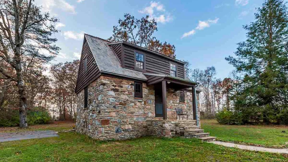Cabin made of a stone and wood, surrounded by trees, and stairs leading to front door