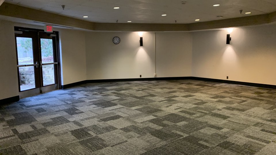 A large carpeted meeting room with wall sconces, double doors to the outside, and no furniture.