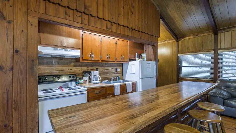 Wooden kitchen with an island, wooden bar stools, white stove, white fridge, cabinets, and sink