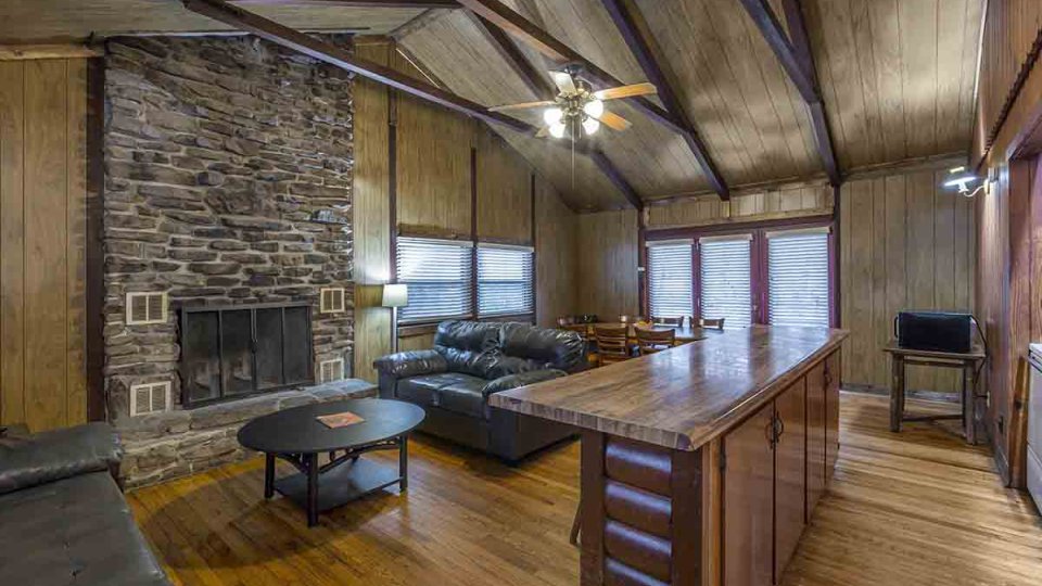 wooden living room with stone fire place, two couches, a coffee table, and windows