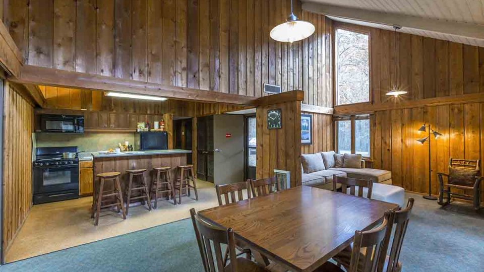 Kitchen and wooden living room with island, bar stools, dining table, chairs, over head lighting, white couch, and lamp