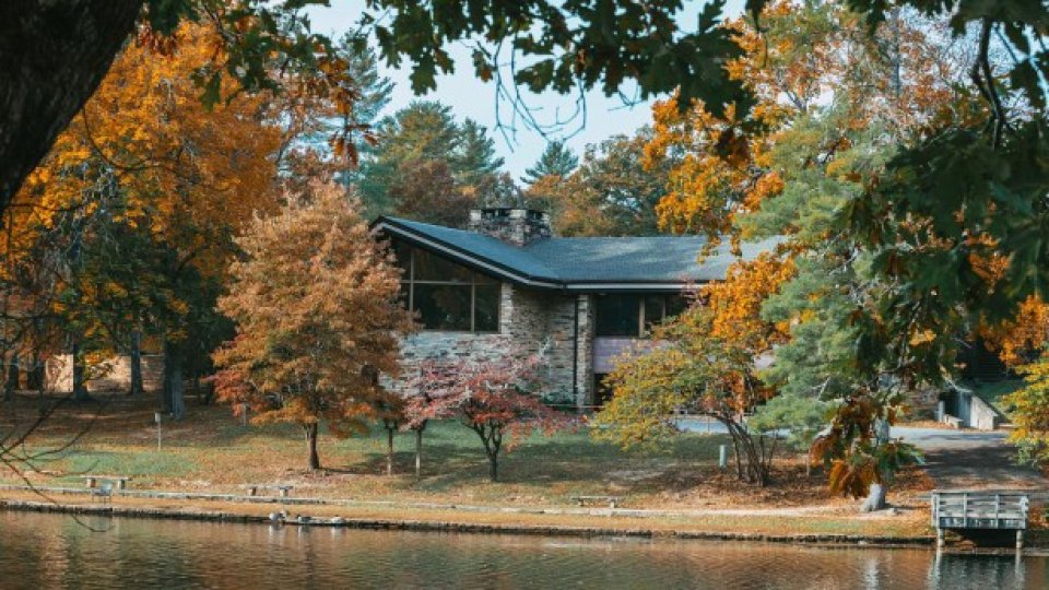 Scenic view of a stone and wood restaurant building surrounded by vibrant autumn trees, reflected in the calm waters of the lake.