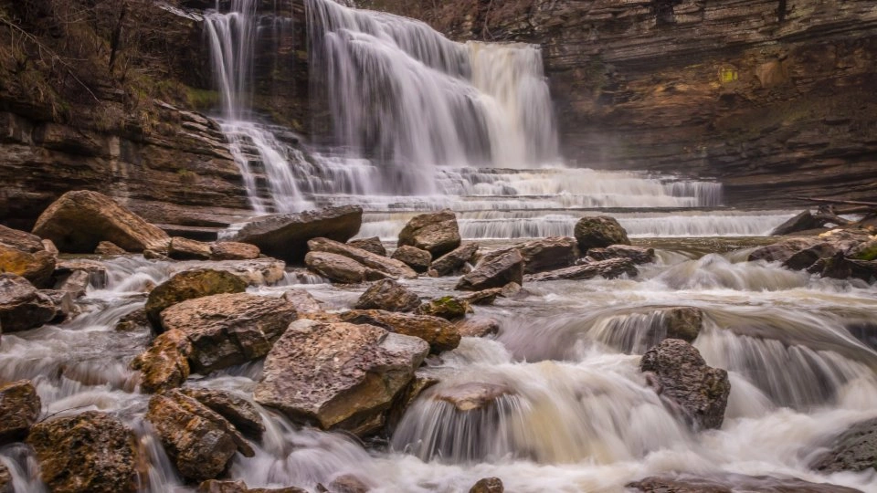 Waterfall cascading over rocky ledges with surrounding cliffs.