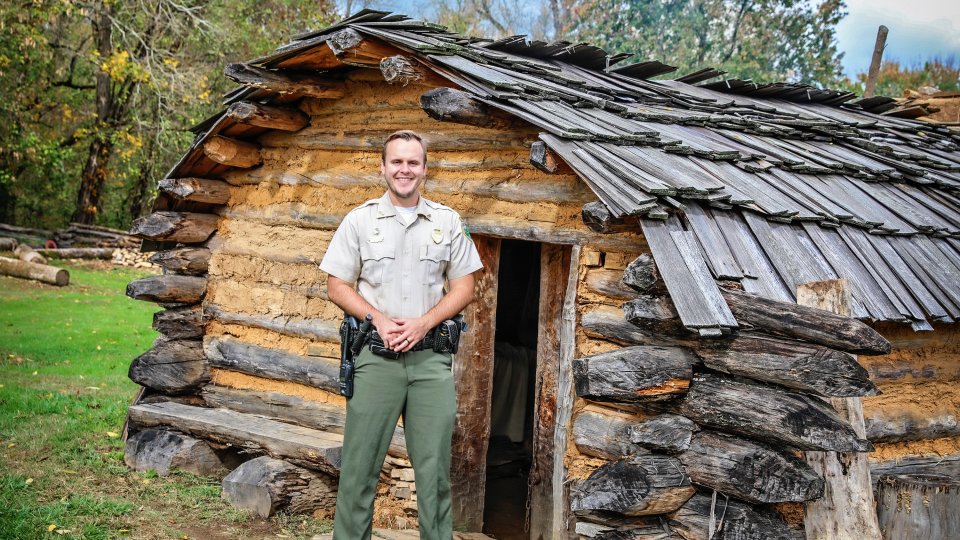 Ranger standing in front of David Crockett historical wooden cabin