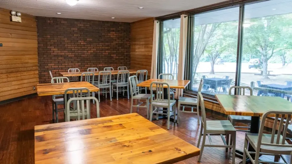 Cafe interior with wooden tables, metal chairs, and large windows.