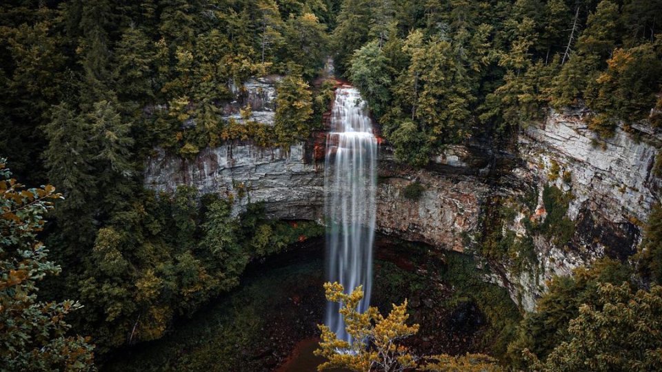 A tall waterfall cascades over a rocky cliff surrounded by dense green forest, creating a serene and majestic natural landscape.