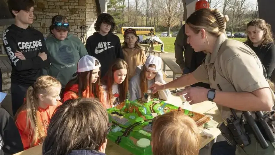 Children gathered around a table watching a park ranger demonstrate something.