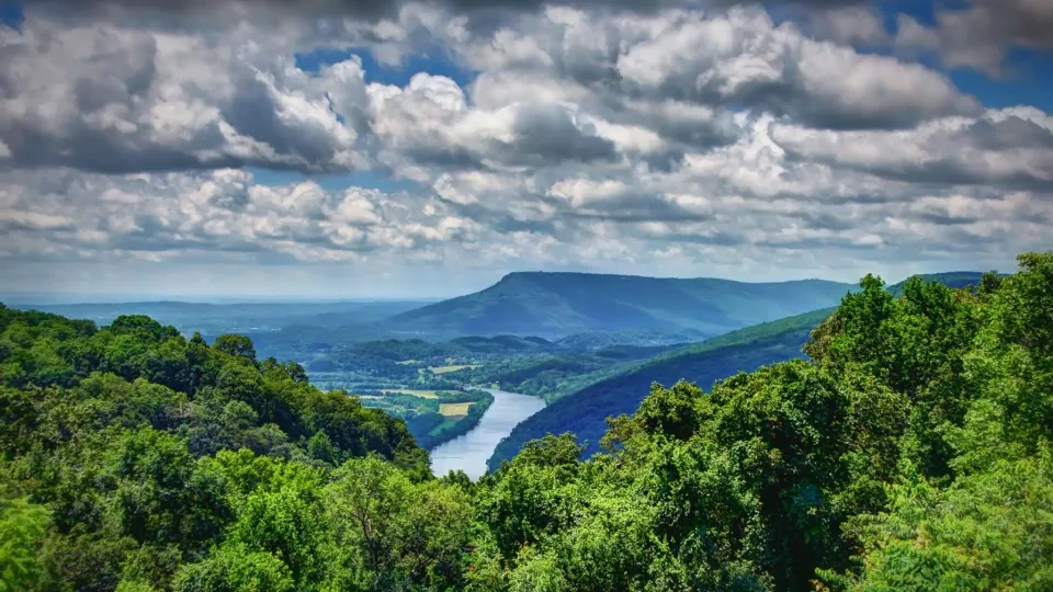 Lush green hills with a winding river under a cloudy sky.