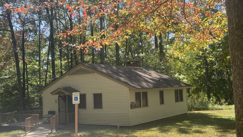 A small, beige cabin with a sloped roof. A ramp and handicap sign are visible in front.