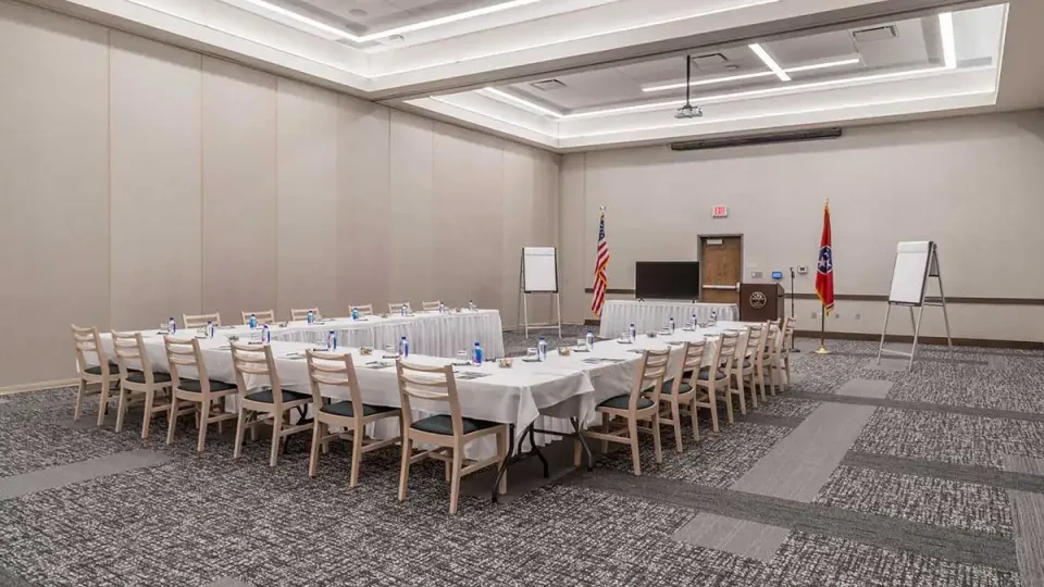 Conference room with a U-shaped table, chairs, flags, and a podium.