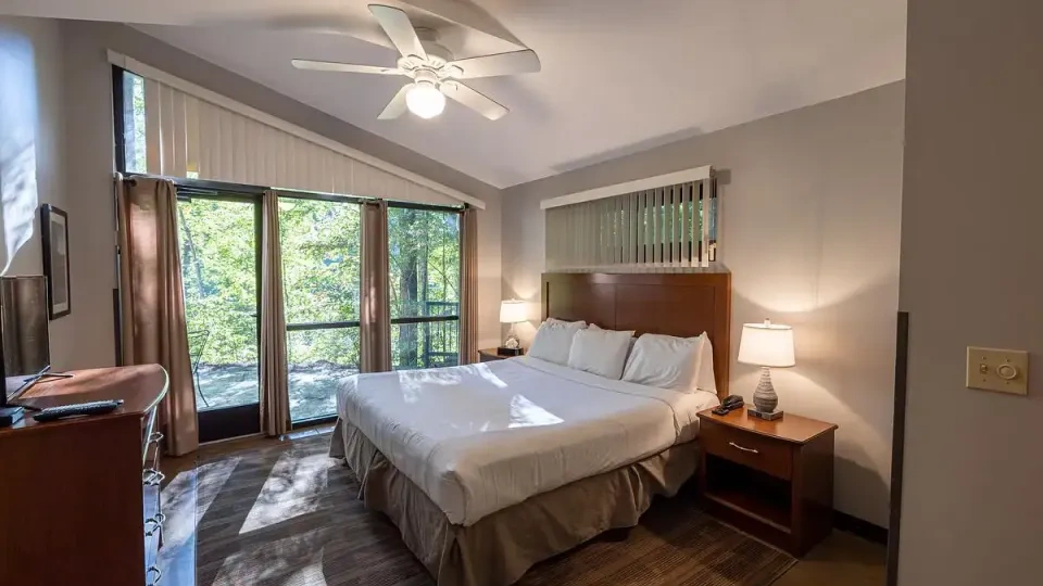 Cozy bedroom with a large bed, ceiling fan, and window view of trees.
