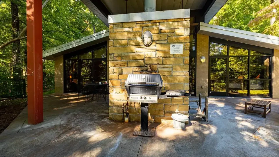 Stone patio with a grill, surrounded by trees and a modern glass building.