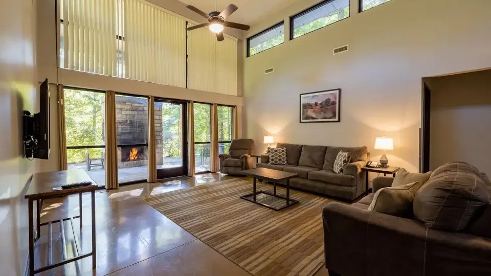 Spacious living room with large windows, sofas, and a glowing fireplace.